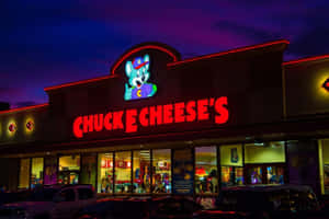 夜間亮燈的 Chuck E Cheese's 遊戲機中心建築，外面停有汽車。 — 查克芝士 壁紙