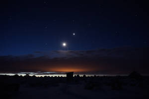 夜晚的雪沙漠景觀，有星星、月亮和橙色地平線光芒。 — 月亮與星星 壁紙