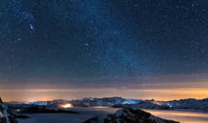 在繁星點點的夜空下，積雪的山脈伴隨著發光的極光和遠處的燈光。 — 暮光 壁紙