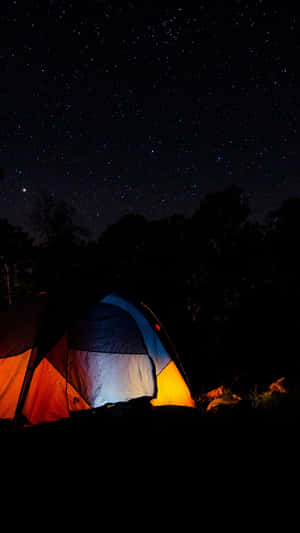 在繁星點點的夜空下，被樹木環繞的明亮帳篷。 — 黑夜 壁紙