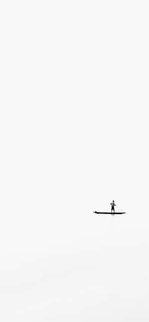 一個人在蒼白的天空下，在廣闊平靜的白色水面上划槳板。 — 白色 iPhone 壁紙