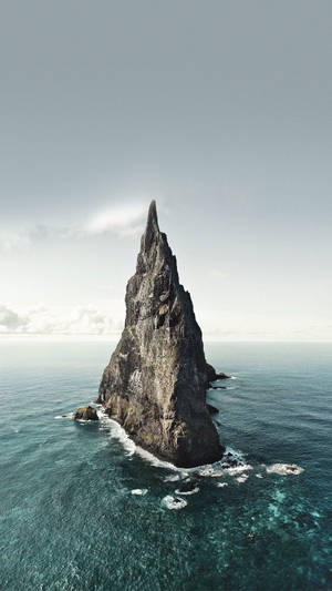 在陰天之下，一座孤獨地矗立在海中的高聳岩石島嶼。 — 海景 壁紙