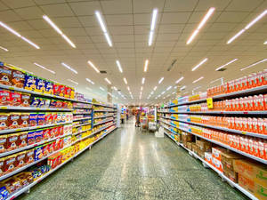 在螢光燈下，貨架上擺滿零食產品的長長超市通道。 — 雜貨店 壁紙