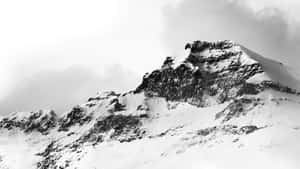 在陰天之下，一個積雪覆蓋、岩石露頭的山峰。 — 冬季美學 壁紙