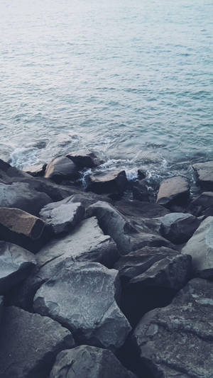 海浪在海洋岸邊的深灰色岩石上破碎。 — iPhone 6s Plus 壁紙