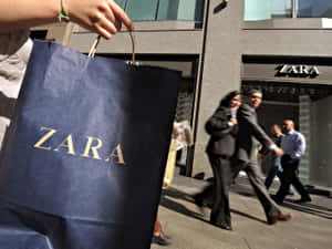 在繁忙的城市人行道上，一名行人手持Zara購物袋。 — Zara 壁紙