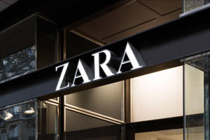ZARA商店標誌在夜間亮起，配有玻璃外牆和深色金屬框架。 — Zara 壁紙
