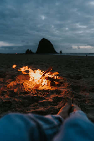 人在黃昏的海灘營火旁放鬆，背景有海蝕柱。 — 黃昏 壁紙