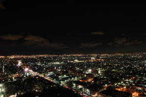 多雲天空下，密集燈光的城市夜景，街道和建築物閃閃發光。 — 晚安 壁紙