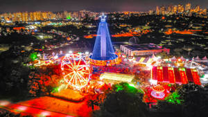 夜晚的節日遊樂園，背景是發光的遊樂設施和城市燈光。 — 城市 壁紙