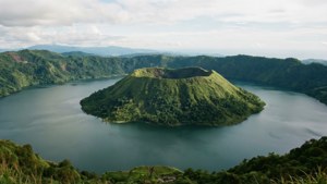 多雲天空下，森林覆蓋的山丘環繞的湖中火山島 — 1280x720 壁紙