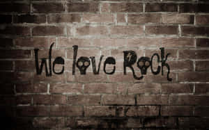 磚牆上的塗鴉寫著 We love Rock，帶有骷髏眼睛和閃電。 — 音樂美學 壁紙