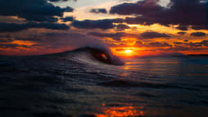 一道強勁的海浪在鮮豔的夕陽下形成管狀。 — 海洋藍 壁紙