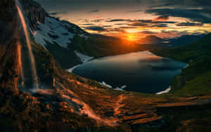 夕陽下，瀑布流入被山脈環繞的湖泊。 — 山脈 壁紙