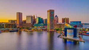 夕陽下的城市天際線，水面倒影和現代建築。 — 日落 壁紙