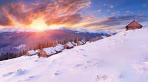 夕陽下白雪覆蓋的山村，有木屋。 — 冬季風景 壁紙