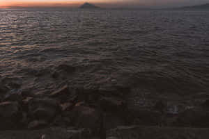 黃昏時分的岩石海岸，海浪和遠山在夕陽餘暉下 — 暮光 壁紙