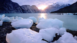 冰山在岩石海岸上休息，太陽在雪山後方落下。 — 海景 壁紙
