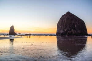 夕陽下的Haystack Rock和海蝕柱，沙灘上有人。 — 俄勒岡州 壁紙