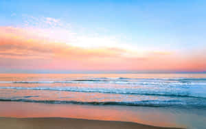 海洋上的夕陽，粉紅色和藍色的天空映照在溫柔的海浪和沙灘上。 — 海灘美學 壁紙