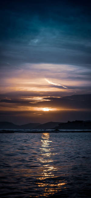 海上的夕陽，帶有金色倒影和暗色山丘 — iPhone 18 壁紙