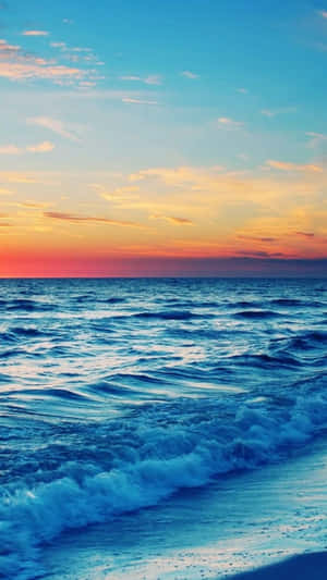 夕陽下，海浪拍打海岸，天空呈現鮮豔的橙色和藍色。 — 海灘 壁紙
