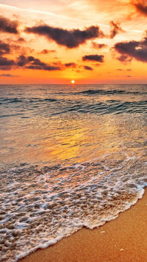 夕陽下的海洋，海浪沖刷沙灘 — 海灘 iPhone 壁紙