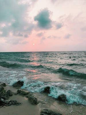 夕陽映照海洋，海浪在黃昏時拍打岩石海灘 — 海灘 iPhone 壁紙