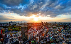 夕陽下，密集的城市景觀中摩天大樓和住宅建築在戲劇性的雲層下。 — 東京 壁紙