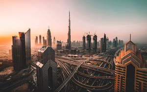 杜拜天際線在夕陽下，高聳的摩天大樓和複雜的高速公路立交橋。 — 城市風景 壁紙