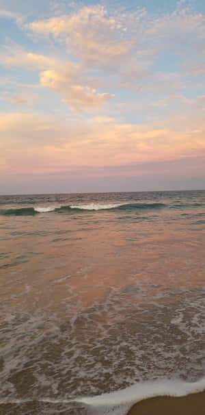 夕陽下的海浪，粉紅色和藍色的天空倒映在水面上。 — 18:9 壁紙