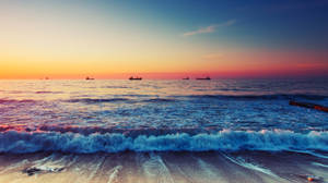 海洋上的日落，海浪拍打海岸，遠處有船隻 — 海灘 壁紙