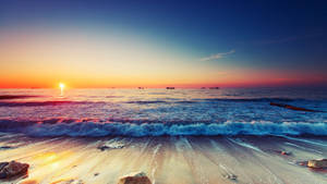 夕陽下的海洋，海浪拍打沙灘，遠處船隻 — 極高畫質 壁紙