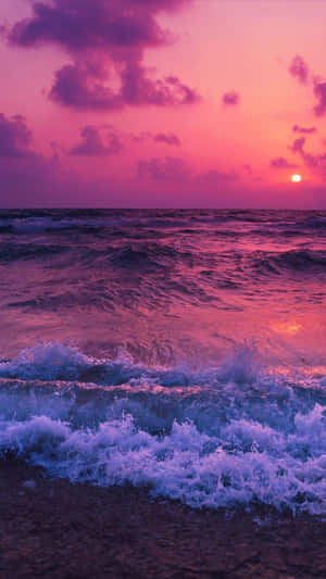 粉紅色和紫色的夕陽映照在海浪上，拍打著海岸。 — 海灘日落 壁紙