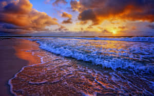 海浪在 vibrant 的夕陽下拍打沙灘。 — 16:10 壁紙