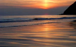 夕陽下的海洋，懸崖附近濕沙上的海浪 — 海灘日落 壁紙