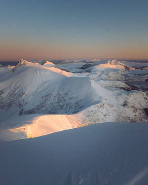 夕陽下積雪山脈，山峰金色光芒，天空清澈 — 丘陵景觀 壁紙