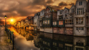 金色夕陽下，運河房屋倒映在水中，有鵝卵石小徑和路燈。