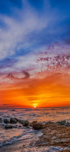 夕陽映照海洋，海浪拍打岩石海岸 — Galaxy A54 壁紙