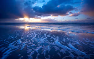 夕陽映照海洋，泡沫海浪和戲劇性的雲層反射金色光芒。 — 海洋桌面 壁紙