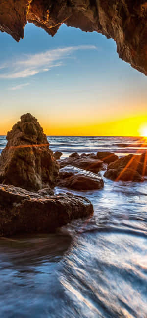 從海蝕洞內觀看的夕陽，海浪拍打岩石。 — Galaxy A55 壁紙
