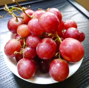 一碗飽滿的紅葡萄放在深色木質表面上。 — 柳橙 壁紙