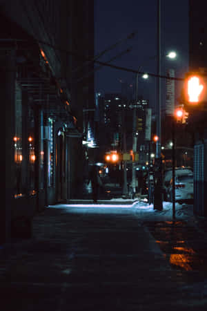 一個人在夜晚的積雪人行道上，在紅色交通號誌下獨自行走。 — 暮光 壁紙