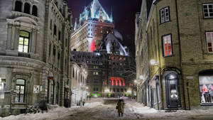 夜晚，一個人在積雪的城市街道上走向燈火通明的歷史建築。 — 城市 壁紙