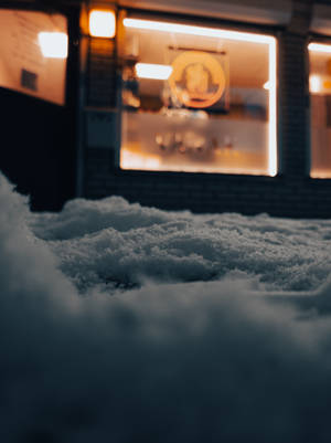 夜晚，燈光商店櫥窗前積雪的地面。 — Google Pixel 3 壁紙