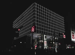 夜晚中一座現代建築，帶有發光的白色網格線和紅色Uniqlo標誌。 — 中性 壁紙