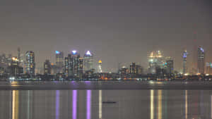 夜晚城市天際線，發光的建築物倒映在平靜的水面上，還有一艘小船。 — 孟買 壁紙