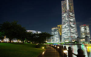 城市夜景，河邊有一座高聳發光的摩天大樓和照明步道。 — 東京鐵塔 壁紙