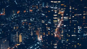 從空中視角看到的夜間城市景觀，帶有發光的窗戶和照明街道。 — iMac 壁紙