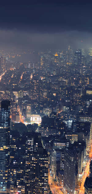 夜晚城市景觀，密集的摩天大樓和發光的窗戶，在烏雲下。 — iPhone 18 壁紙